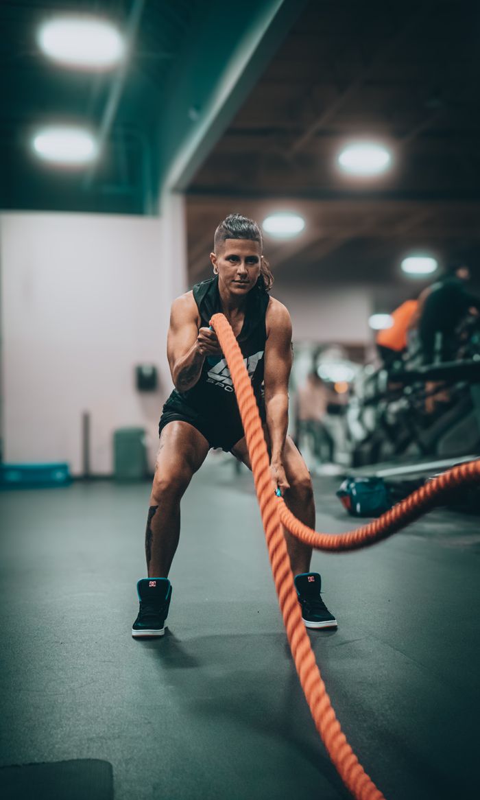 about-01 Athletic person performing an intense battle rope exercise in a modern gym setting.