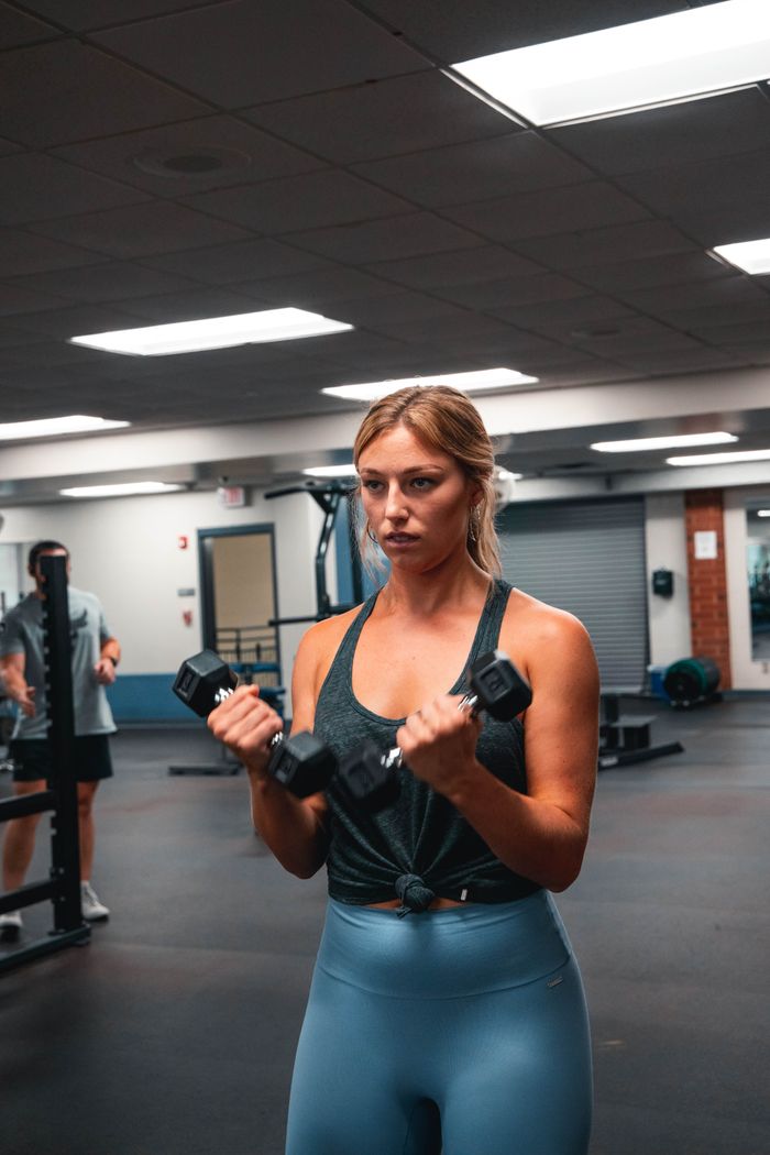 why-choose-us Woman performing bicep curls with dumbbells in a well-lit gym environment.